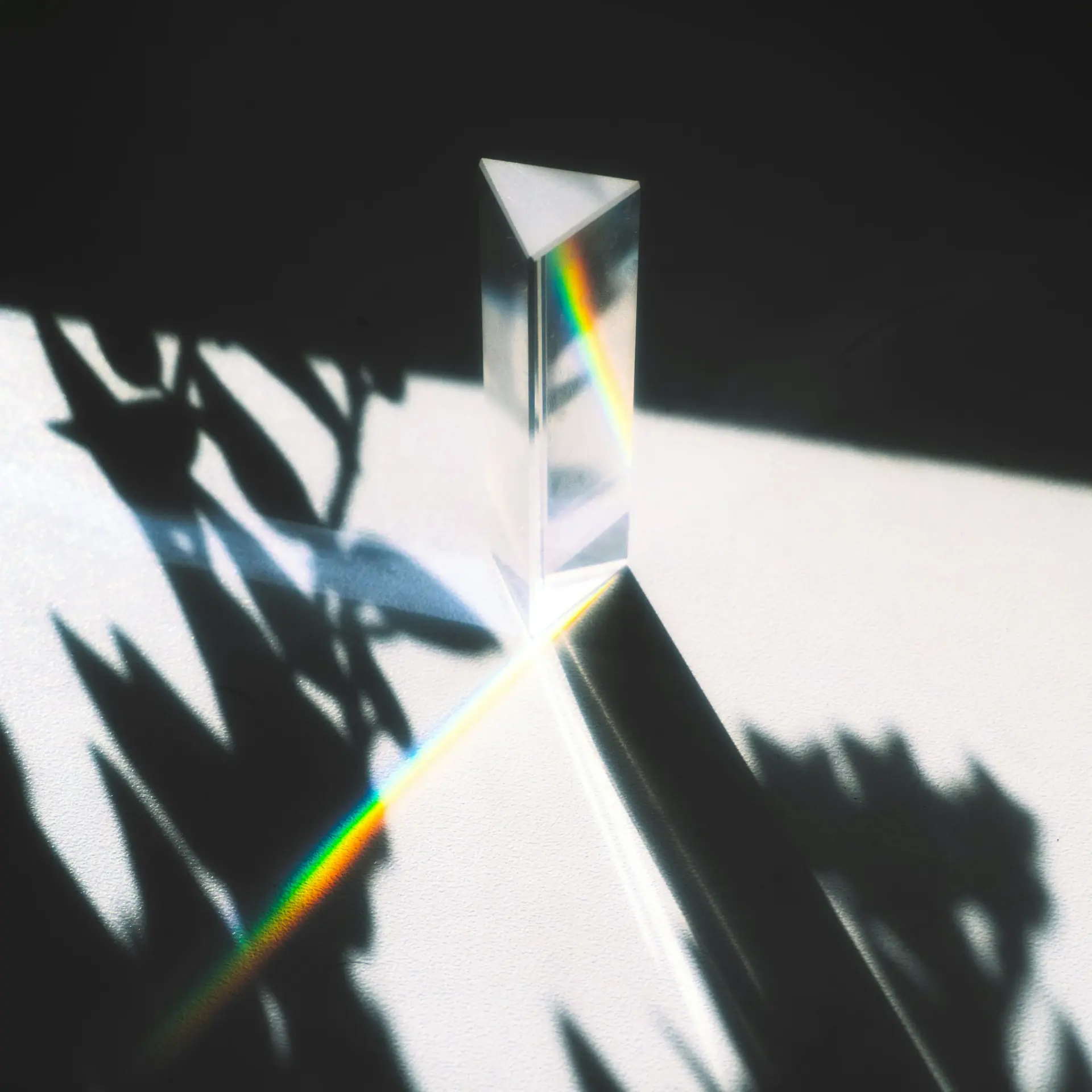 A glass prism separating sunlight into a rainbow among crisp leaf shadows